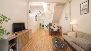 A modern living room with a flat-screen TV, wooden flooring, a dining area with a table and chairs, a sofa, and a staircase leading to an upper level. - Siam Place Family House Near Khaosan 8 Guests (Bangkok)