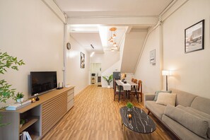 Ein modernes Wohnzimmer mit Flachbildfernseher, Holzboden, einem Essbereich mit Tisch und Stühlen, einer Couch und einer Treppe, die in ein Obergeschoss führt.