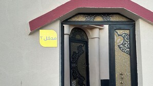 Entrada de un edificio con una puerta decorativa, un letrero amarillo con texto árabe y un tejado rojo.