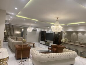 A modern living room with a sofa, armchairs, a coffee table, and a TV. - Luxury 5-Bedroom Apartment with 5 Bathrooms and Private Courtyard 
شقة فخمة (Jeddah)