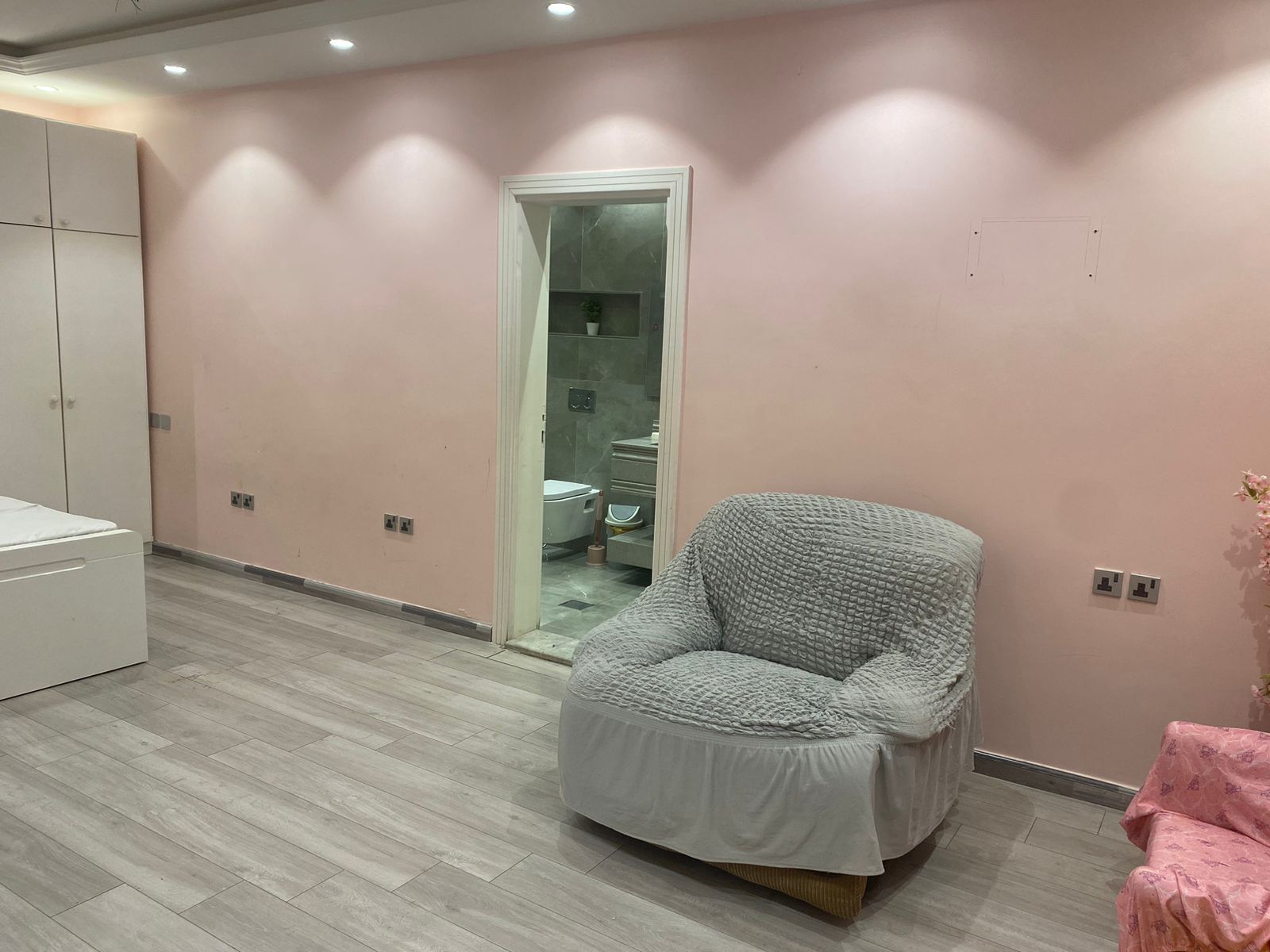 Habitación con un armario amplio, una silla mullida y un baño visible a través de una puerta.