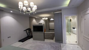 A bedroom with a treadmill, a TV, a minibar, and a bathroom visible through an open door. - Luxury 5-Bedroom Apartment with 5 Bathrooms and Private Courtyard 
شقة فخمة (Jeddah)