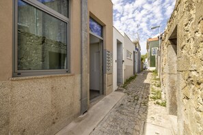 Eine enge Kopfsteinpflasterstraße, begrenzt von Gebäuden mit großen Fenstern und einer Steinmauer.