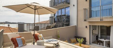 Une terrasse sur le toit, avec des chaises longues, une table et un grand parasol.