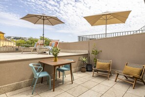 Eine Terrassenanlage im Freien mit Tisch, Stühlen, zwei Sonnenschirmen und Kübelpflanzen.