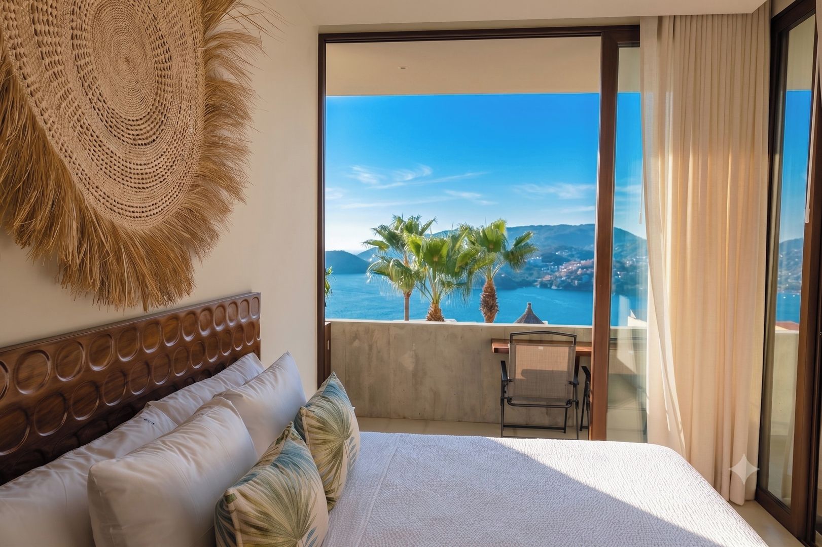 A bedroom with a large bed, a view of the sea, and a balcony with palm trees.