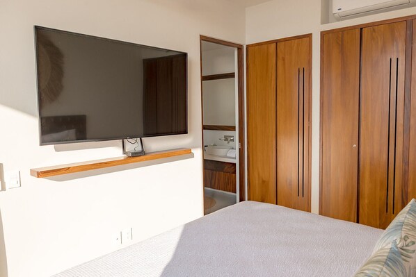 A bedroom with a bed, a TV mounted on the wall, wooden wardrobes, and a built-in shelf.