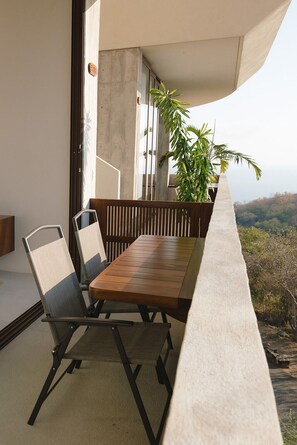 A balcony with a wooden table and chairs, a potted plant, and a view of the landscape.