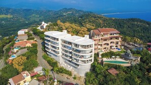 A multi-story hotel with balconies, a swimming pool, and a view of the surrounding hills and coastline. - Studio Villa at Cerro del Vigia (Zihuatanejo)