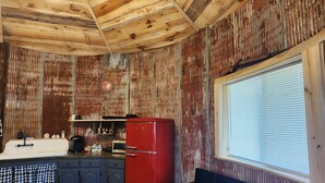 Een rustiek interieur met zichtbare houten balken, een rode koelkast, een donkerblauwe bank en een keuken met een spoelbak en kastjes.