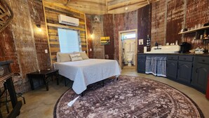 Een rustieke kamer met een bed, een rond vloerkleed, een houten plafond en een kitchenette.