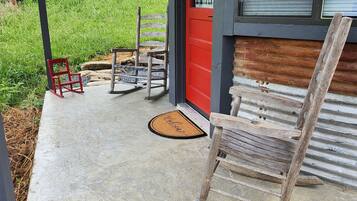 A covered porch with a red door, a wooden rocking chair, and a bench.