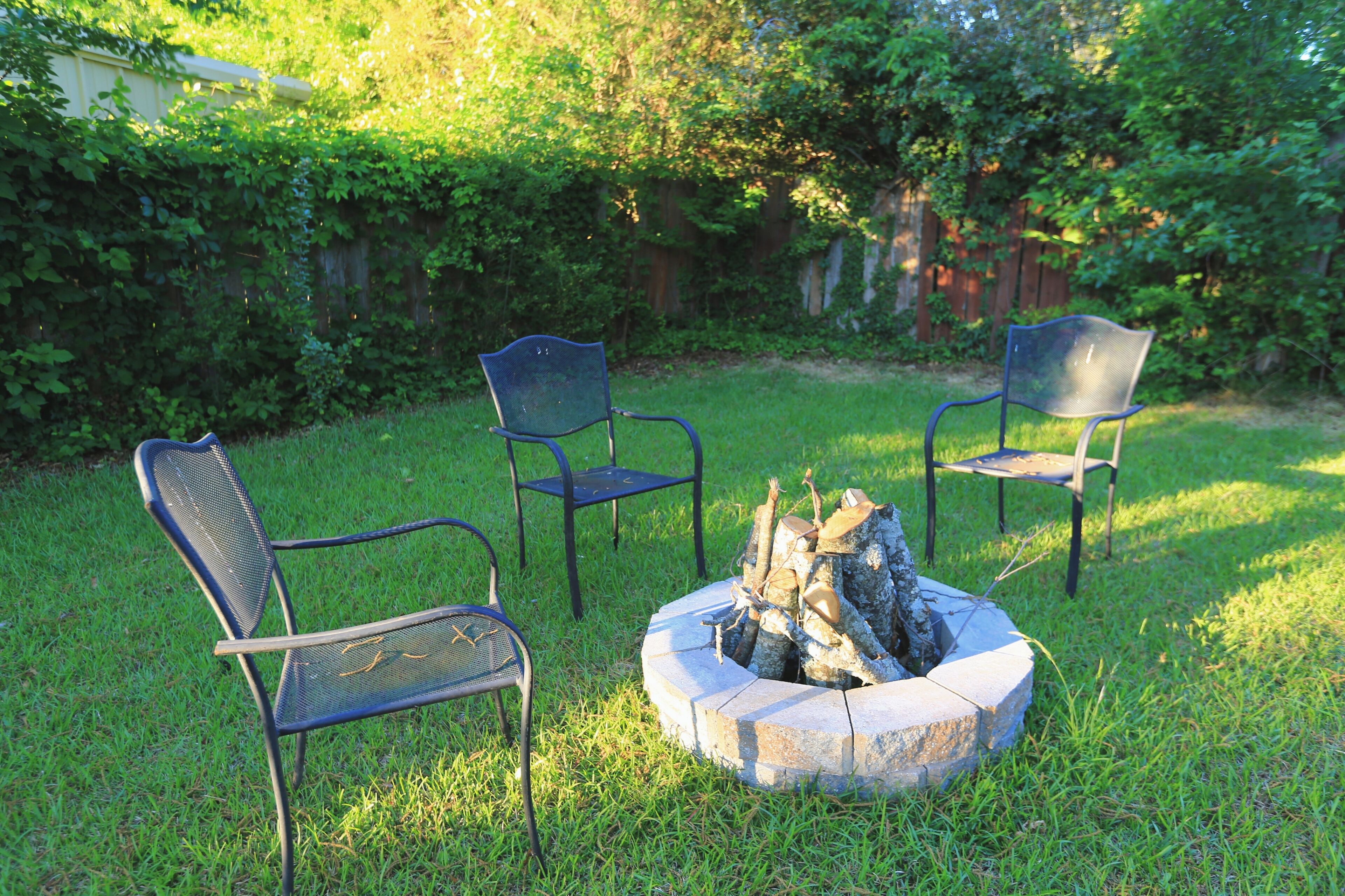 A backyard with a fire pit surrounded by metal chairs.