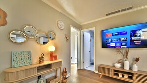 A living room with a flat-screen TV mounted on the wall, a wooden console table with decorative items, and a hallway leading to another room.