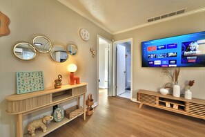 A living room with a flat-screen TV mounted on the wall, a wooden console table with decorative items, and a hallway leading to another room.