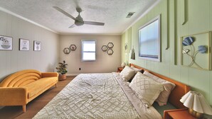 A bedroom with a bed, a sofa, a ceiling fan, and wall decorations.