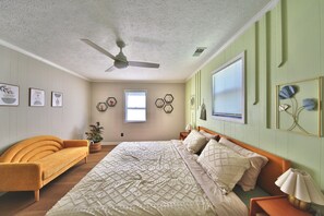 A bedroom with a bed, a sofa, a ceiling fan, and wall decorations.
