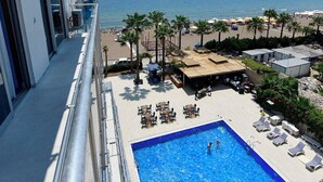 A pool area with a view of the beach and ocean, lounge chairs, and a clear sky. - Mediterranean Resort Hotel (Silifke)