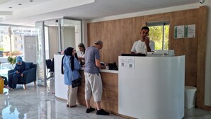 A reception area with a reception desk, seating area with blue sofas, and a view of the street outside. - Mediterranean Resort Hotel (Silifke)
