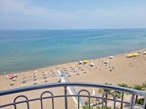 Una playa con sombrillas y sillas reclinables, cielo despejado y el océano.