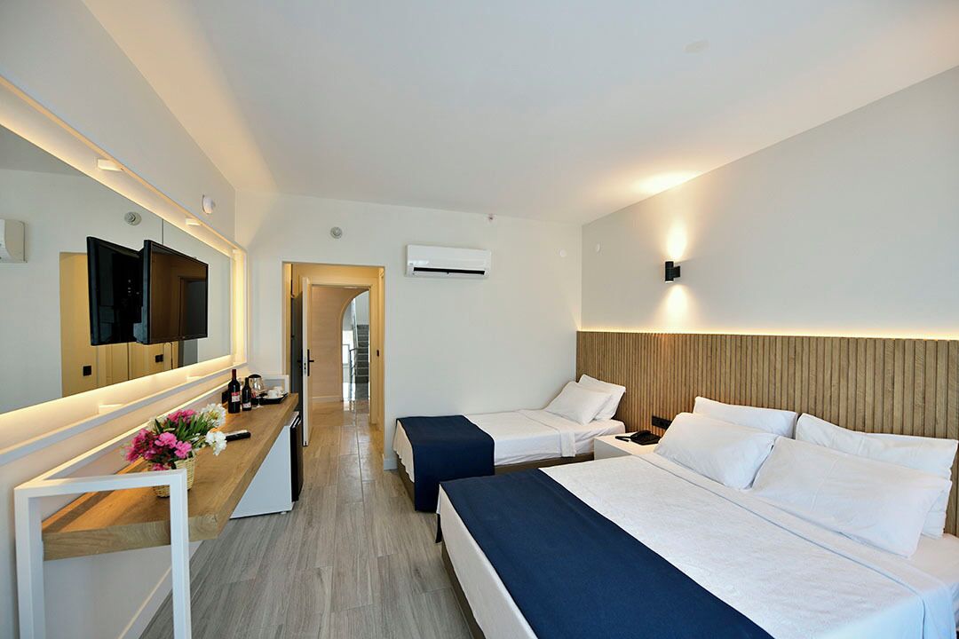 Habitación de hotel con dos camas, un escritorio, televisor de pantalla plana, espejo y aire acondicionado instalado en la pared.