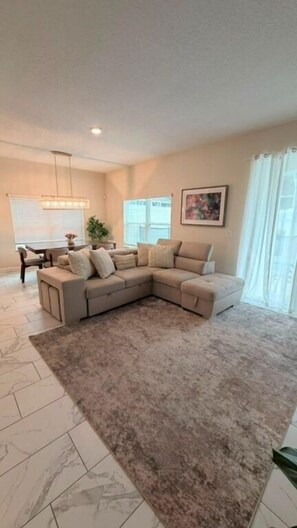A living room with a sectional sofa, a dining table, and a chandelier. - 5 BD / 4 BA / Champions Gate (444 OC) (Kissimmee)