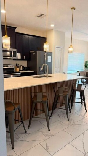 A modern kitchen with a central island, bar stools, pendant lighting, and dark cabinetry. - 5 BD / 4 BA / Champions Gate (444 OC) (Kissimmee)