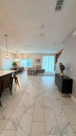 A spacious living area with a dining table and chairs, a sofa, and a staircase leading to an upper level. - 5 BD / 4 BA / Champions Gate (444 OC) (Kissimmee)