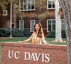 A person standing in front of a brick wall with the letters 'UC DAVIS' on it.