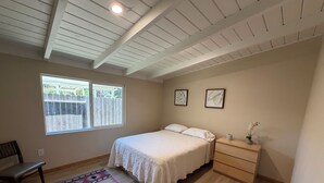 A bedroom with a bed, bedside table, nightstand, and a window with a view of a wooden fence.