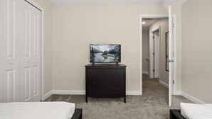 Un dormitorio con dos camas, un tocador y un televisor sobre un mueble.