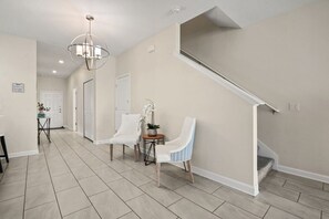 A spacious hallway with a staircase, two chairs, a small table with a plant, and a door. - 5 BD/ 4 BA/ Storey Lake (4810 ML) (Kissimmee)
