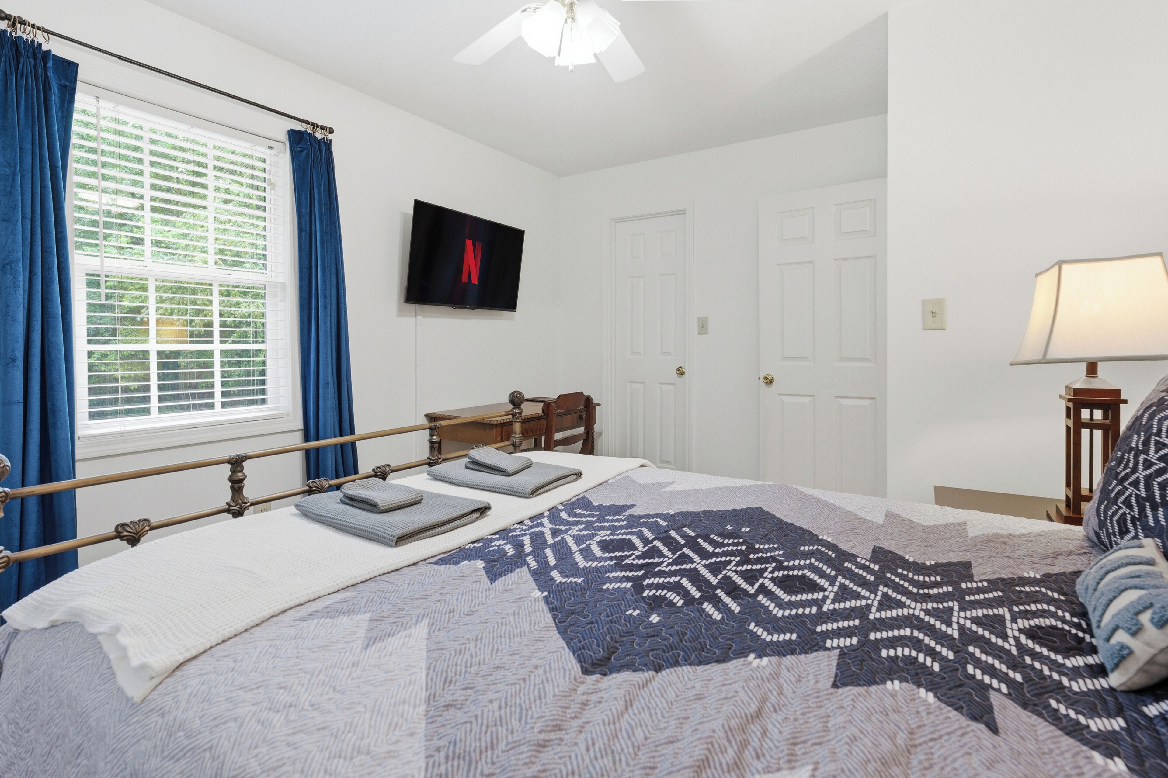A bedroom with a bed, a television mounted on the wall, a window with curtains, and a door.