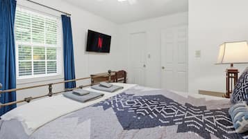 A bedroom with a bed, a television mounted on the wall, a window with curtains, and a door.