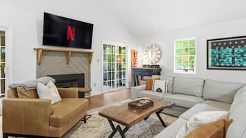 Una sala de estar con chimenea, televisor montado en la pared, sofá, mesa de centro y un reloj en la pared.