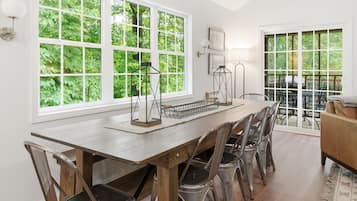 Un comedor con una larga mesa de madera, sillas de metal y vistas a la vegetación a través de amplios ventanales.