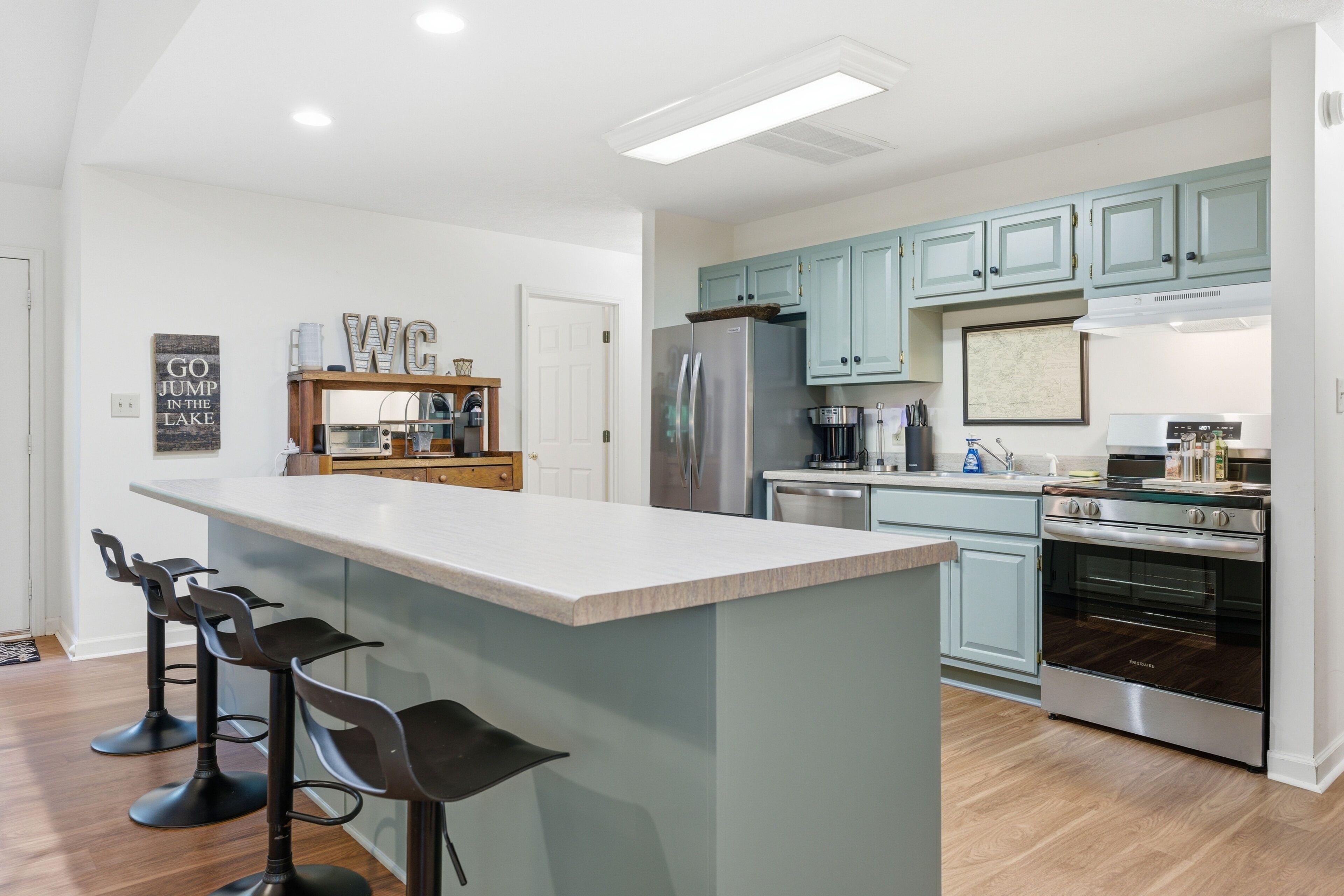 A modern kitchen with a central island, bar stools, a refrigerator, a stove, and light blue cabinets.