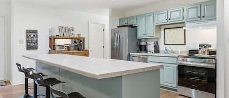 A modern kitchen with a central island, bar stools, a refrigerator, a stove, and light blue cabinets.