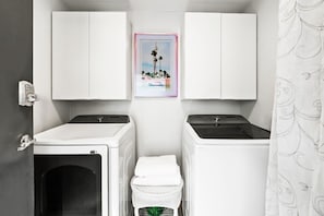 Ein Waschraum mit zwei Waschmaschinen, einem Wäscheständer und einem Bild an der Wand.
