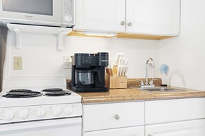 Eine Küche mit Herd, Kaffeemaschine, einem Messerblock und einer Mikrowelle.