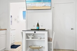 A small dining area with a table, a chair, a wine bottle, and a TV screen displaying a beach scene. - Beach Rd, 300ft to Beach Access & 500ft to Siesta Key Village, Studio (Siesta Key)