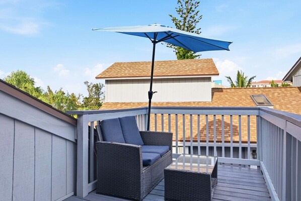 Una terraza con mobiliario de mimbre y una sombrilla azul.