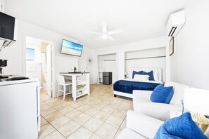 Ein modernes Hotelzimmer mit Bett, weißem Sofa, Schreibtisch mit Stuhl, Fernseher und Deckenventilator.