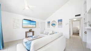 A spacious living room with a white sofa, a flat-screen TV, and artwork on the walls.