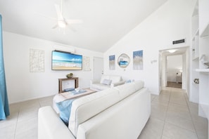 A spacious living room with a white sofa, a flat-screen TV, and artwork on the walls.