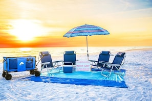 A beach scene with a cart labeled 'Oceanic Travel,' two beach chairs, a striped umbrella, and a sign listing beach gear.