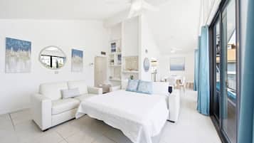 A modern hotel room with a bed, a sofa, a dining area, and a view through a glass door.