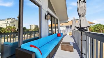 Un balcon avec un canapé bleu, une lanterne et une pergola agrémentée de parasols.