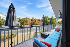 A balcony with a blue sofa and red cushions, a metal railing, and umbrellas.