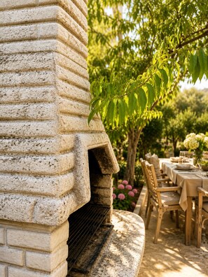Una parrilla de piedra con chimenea, rodeada de mesas y sillas para comer al aire libre.